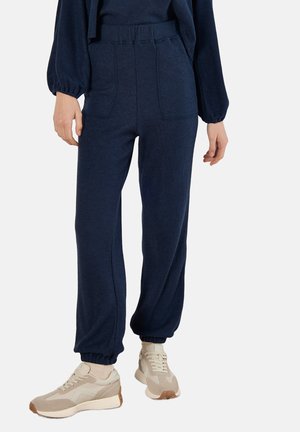 Navyblaue Jogginghosen aus strukturiertem Stoff, mit hohem Bund, Seitentaschen und elastischen Bündchen, kombiniert mit beigen Sneakers.