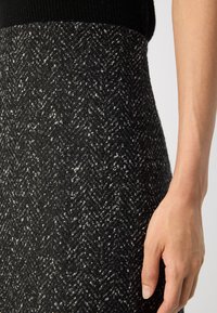 Gros plan d'une main reposant à côté d'une jupe en chevrons texturée noir et blanc portée avec un haut noir.