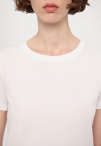 Tricou alb din bumbac cu guler rotund, având un logo "Armani Exchange" brodat subtil în centru. Mâneci scurte și textură ușoară.