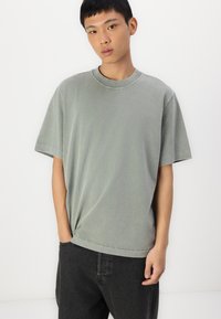 T-shirt de algodão cinza com decote redondo e mangas curtas, apresentando um corte descontraído e uma textura subtil, combinada com jeans pretos.
