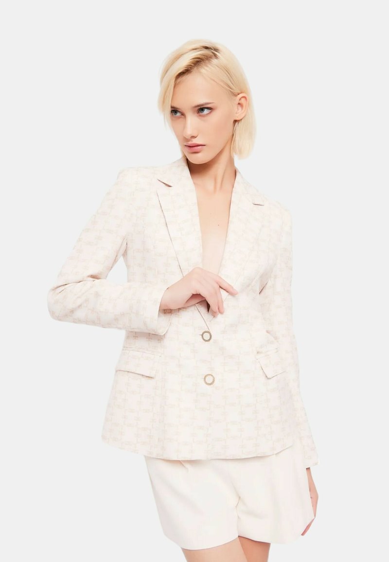 Lichtbeige blazer met een subtiele, gepatroniseerde textuur, dubbele knopen, gelidetaille met steekzakken en decoratieve knopen in goudkleur.