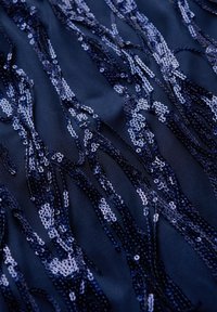Navy mesh fabric with cascading sequins in various shades creates a textured pattern, featuring shimmering accents against a dark background.