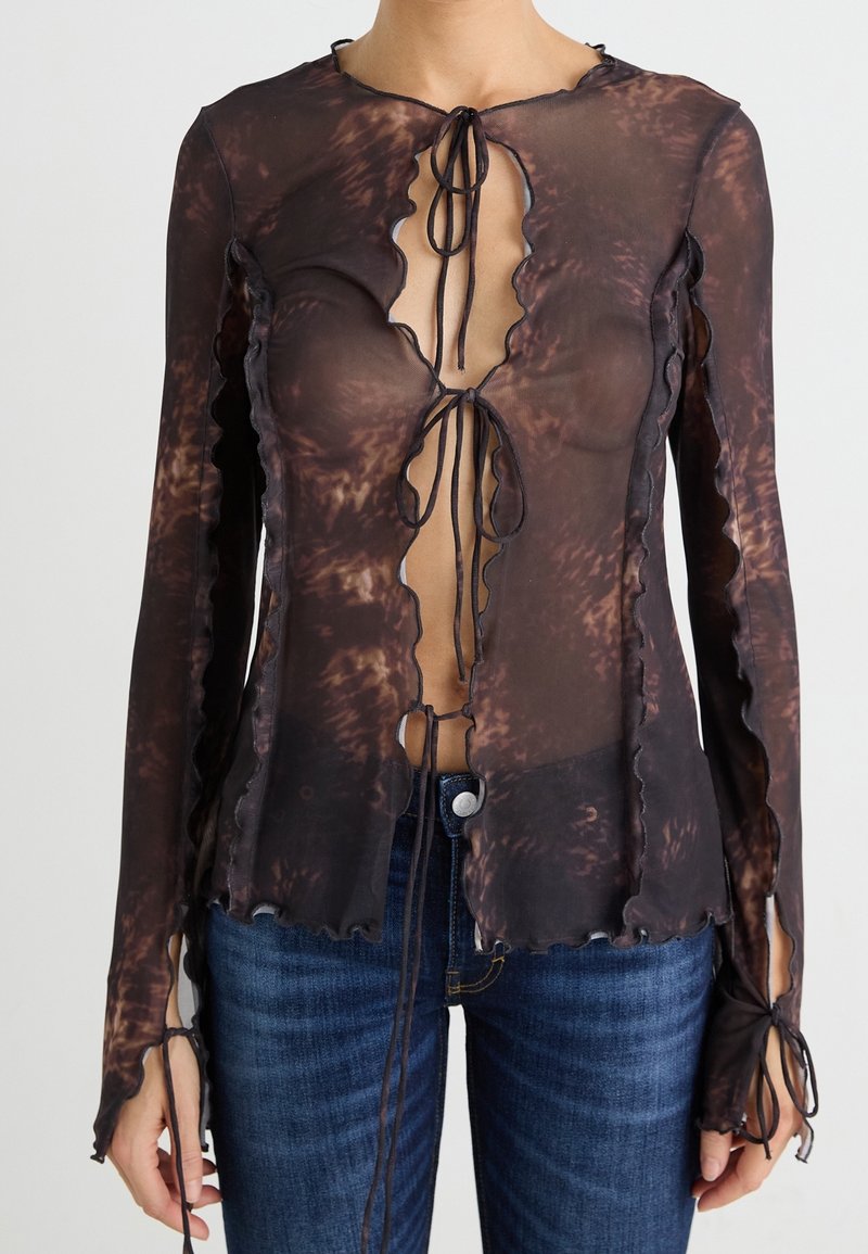 Top noir transparent à manches longues avec un ourlet ondulé, un décolleté profond et des fermetures à nouer. Présente un motif marbré marron et une coupe ajustée.