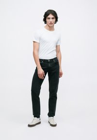 Sorte denim jeans parret med en hvid bomulds t-shirt. Model iført hvide sneakers. Enkel design, almindelig pasform, ingen synlige mønstre eller logoer.