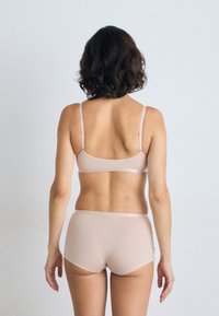 Vaaleanbeige bralette ja korkeavyötäröiset alushousut, jotka on valmistettu sileästä kankaasta. Ne sisältävät säädettävät hihnat ja minimalistisen muotoilun.