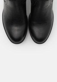 Bottes noires en cuir à la cheville avec une finition lisse, bout rond et détails de couture subtils autour des bords. Semelle plate pour un confort optimal.