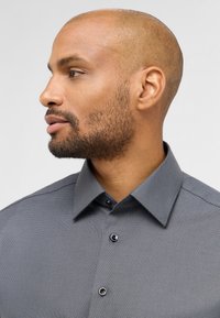 Antracit knap-op skjorte med et tekstureret mønster, spread krave og sorte knapper. Sideprofil af en person iført den.