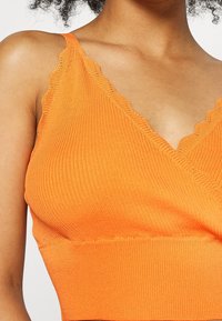 Hedvábný oranžový bralet s vroubkovaným vzorem a zvlněnými okraji, s výstřihem ve tvaru V, opatřený elastickým pásem pro pohodlí a hladkým materiálem.