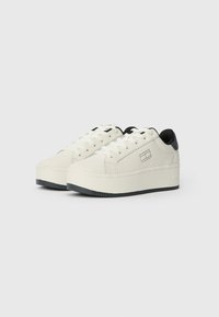 Witte platform sneakers met zwarte hielaccenten, vetersluiting, een gestructureerde rubberen zool en een subtiel merklable op de zijkant.
