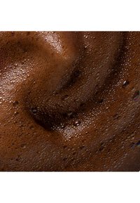 Gros plan sur une mousse de café brun foncé avec des bulles denses et minuscules créant une surface texturée.