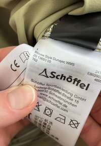 Beiges Textilblusenschild mit schwarzem Markenlogo, Waschsymbolen und Produktdetails, einschließlich "Blusenstil Dunajec WMS" und Größeninformationen.