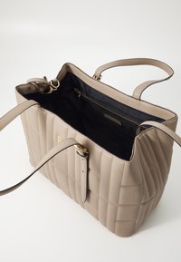 Sac fourre-tout en cuir beige avec un motif matelassé, intérieur doublé noir, poignées doubles et une quincaillerie dorée. Design spacieux avec une poche zippée.