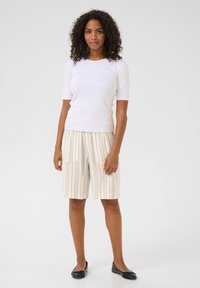 Un haut blanc ajusté à manches courtes associé à un short rayé beige avec deux poches avant. Des ballerines noires complètent la tenue.