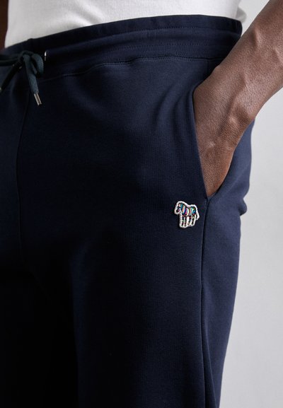 Σκούρες μπλου τζιν φόρμες από υφασμάτινο ύφασμα, με μικρό, πολύχρωμο κεντημένο λογότυπο ζώου στη τσέπη. Ελαστική μέση με κορδόνι.