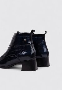 Bottines en cuir verni navy, avec un bout rond, une finition brillante, un petit talon et une languette à l'arrière. Détails avec un accent métallique.