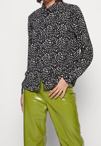 Black button-up shirt with a white polka dot pattern, long sleeves, and a classic collar, paired with shiny green pants.
