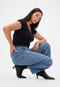 Mustast sobituvast särgist ja kõrge vöökohaga laia mugava jalaga sinistest teksapükstest koosnev komplekt. Mustad terava ninaga pahkluud saab jalutsid täiustavad välimust. Minimalistlik taust.