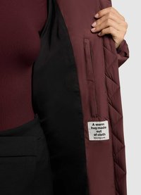 Burgundy steppelt dzseki belseje, fekete béléssel és feliratos címkével. A bal oldalon egy zseb látható belül.