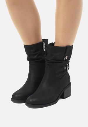 Botas de tobillo negras de cuero sintético, con un diseño de puño doblado, cremallera lateral y tacón tipo bloque para un soporte estable.