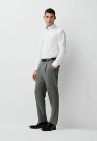 White long-sleeve shirt with a pointed collar, paired with gray patterned trousers and black glossy shoes. Tailored fit, pocket detail on pants.