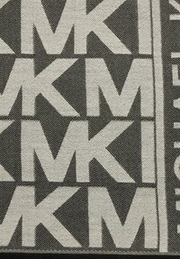 Tessuto che presenta un motivo geometrico nero e crema di lettere "MK" ripetute in grassetto, su uno sfondo texture con bordi frangiati.