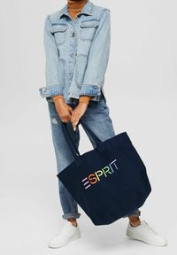Sac fourre-tout en toile bleue marine avec "ESPRIT" en lettres multicolores. Il dispose de deux poignées robustes et d'un intérieur spacieux, idéal pour un usage quotidien.