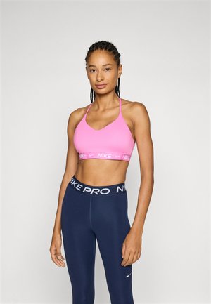 Soutien-gorge de sport rose avec un design en V et des fines bretelles, arborant une bande avec le logo Nike blanc. Associé à un legging taille haute bleu marine.