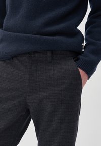Maglione a maglia blu navy con orlo a coste, abbinato a pantaloni a quadri grigio scuro con chiusura a bottoni e tasche laterali. Tessuto morbido, vestibilità slim.