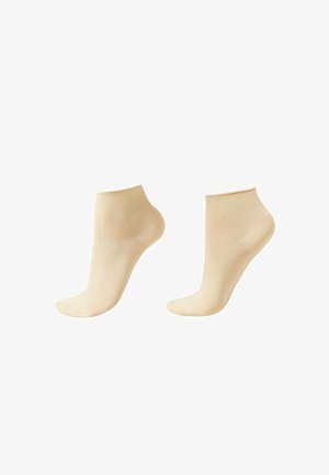 Een paar beige enkelsokken op voetvormige vormen, afgebeeld tegen een witte achtergrond.