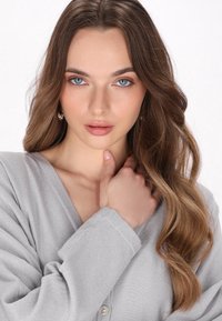 Grijze v-hals cardigan met een zachte textuur, knoopdetails en lange mouwen. Subtiele glans versterkt de stof. Model heeft lang, golvend haar.