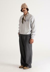 Felpa grigia con logo rotondo, pantaloni a righe neri, scarpe in pelle marroni e un berretto di maglia beige, abbinato a una sciarpa marrone chiaro.