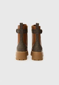 Bottines en cuir marron avec un dos à motifs, semelles en caoutchouc épaisses et détail de fermeture éclair en métal doré, arborant un design robuste et texturé.