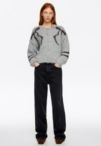 Szary dzianinowy kardigan z okrągłymi guzikami, z ciemnoczerwonymi akcentami i wyrazistymi wzorami. Połączony z czarnymi, wysokim stanem jeansami.