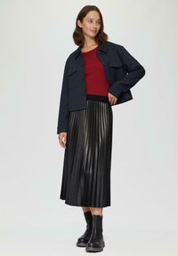 Marine blauwe cropped jas met twee voorzakken, strakke rode ribgebreide top en zwarte geplooide midi rok. Zwarte enkellaarzen maken de outfit compleet.