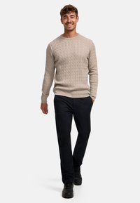 Beige kabelstrikket genser med ribbet rund hals, kombinert med mørke bukser og svarte joggesko; jevn tekstur, tettsittende design.