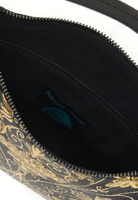 Interno della borsa nera foderato in tessuto, con ornati disegni floreali dorati. Include una cerniera e un'etichetta con la scritta "Made in Italy."