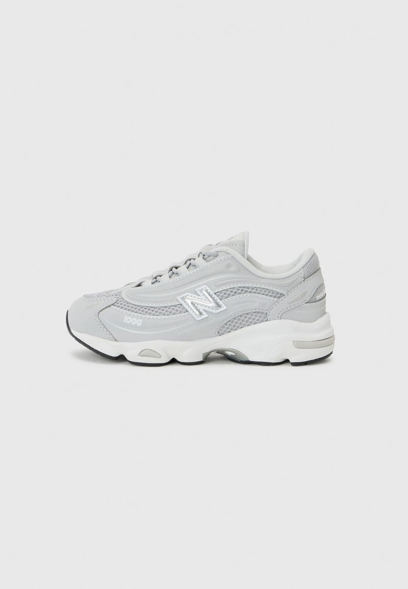 Šedá sportovní bota s síťovinou a syntetickými vrstvami. Má bílou mezipodešev, texturované akcenty, šněrování a logo poblíž paty.