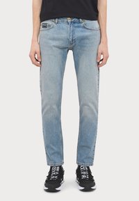 Lyseblå denimjeans med rett passform, med klassisk femlommedesign og knappelukking. Brukt sammen med svarte joggesko.