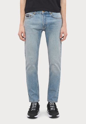 Jeans in denim azzurro chiaro con vestibilità a gamba dritta, caratterizzati da un classico design a cinque tasche e chiusura con bottone. Indossati con sneaker nere.