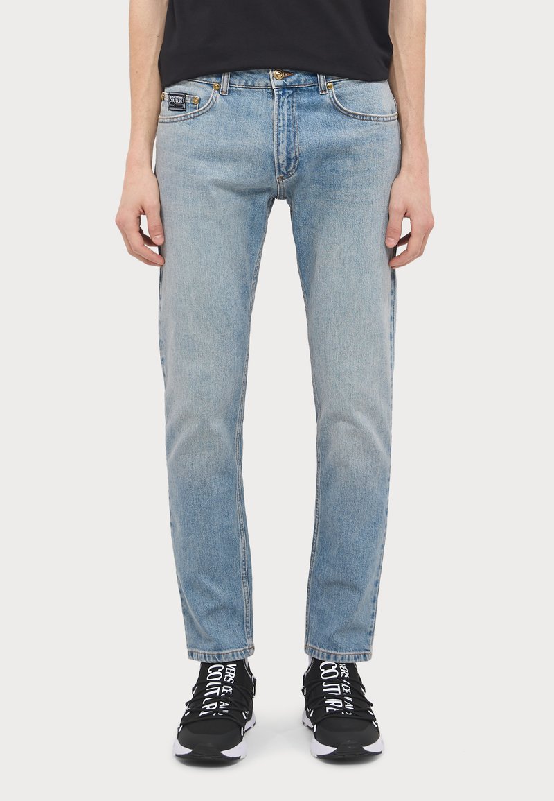 Lyseblå denimjeans med rett passform, med klassisk femlommedesign og knappelukking. Brukt sammen med svarte joggesko.