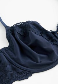 Granatowy biustonosz z gładkiej satynowej tkaniny z koronkowym wykończeniem wzdłuż górnej krawędzi, regulowanymi ramiączkami i miękką teksturą.