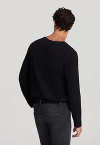 Maglietta nera a maniche lunghe con righe, scollatura ampia e vestibilità comoda; abbinata a jeans grigio scuro con tasche posteriori e vita aderente.