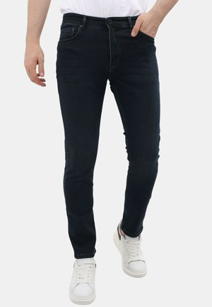 Donkerblauwe denim jeans met een slim fit, voorzien van vijf zakken, een knoop- en ritssluiting, en subtiele stikseldetails. Gecombineerd met witte sneakers.