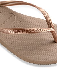 Bronse Havaianas flip-flop med teksturert brun fotseng, med en tynn metallisk stropp og hevet logo langs siden.