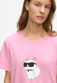 Femeie îmbrăcată cu un tricou roz, pe care este imprimat un pisoi de desene animate alb, purtând ochelari de soare negri.