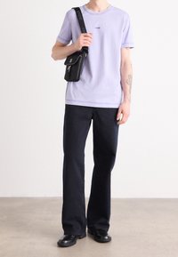 Levandulové bavlněné tričko s malým logem "BOSS", spárované s tmavě modrými zvonovými džínami a černými koženými botami. Obsahuje černou brašnu přes rameno.
