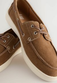 Braune Wildlederschuhe im Boot-Stil mit weißen Nähten, runder Zehenform und beigen Gummisohlen. Verfügt über Leder-Schnürsenkel und Metall-Ösen.