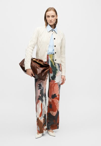 Cardigan crème en maille, chemise bleu clair à col, pantalon jambes larges à imprimé floral avec accents rouges et noirs, et sac en cuir marron.