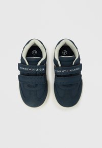 Tmavě modré tenisky pro batolata s pásky na suchý zip, vyrobené z hladkého syntetického materiálu, s bílou podrážkou a logem značky na pásku.