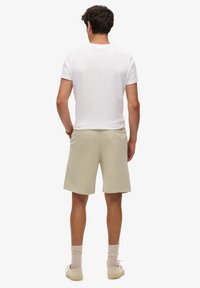 T-shirt bianca da uomo a maniche corte, pantaloni corti in cotone beige e scarpe beige. Vista posteriore che mostra la vestibilità rilassata e i dettagli dell'orlo.